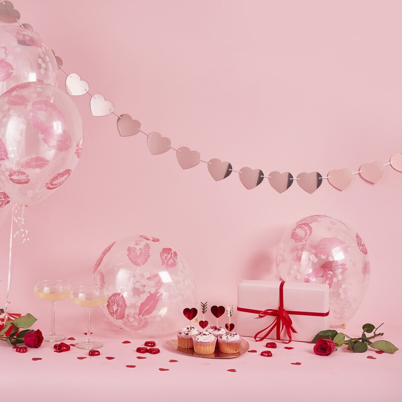 May include: A romantic scene with pink balloons printed with lip imprints, a heart-shaped garland, cupcakes, and a gift box tied with a red ribbon. Scattered red heart confetti and roses complete the Valentine's Day theme.