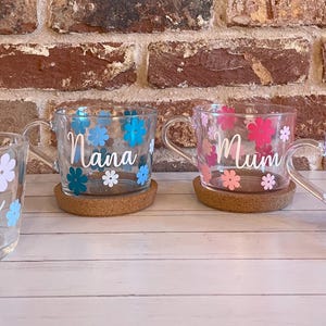 May include: Four glass mugs with floral designs and personalized names. The mugs are "Nanny", "Nana", "Mum", and "Mum". Each mug has a cork coaster.