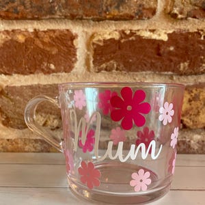 May include: Clear plastic mug with a white "Mum" design and pink and white flower decals.