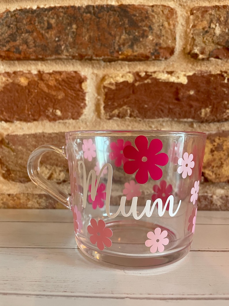 May include: Clear plastic mug with a white "Mum" design and pink and white flower decals.