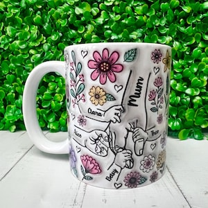 May include: White ceramic mug with a floral design and handprints. The handprints are labelled with the names "Mum", "Alice", "Clara", "Bodsy", and "Theo".