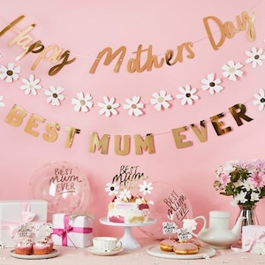 May include: A festive Mother's Day display with gold banners reading "Happy Mothers Day" and "Best Mum Ever." The scene includes a cake, cupcakes, gifts, balloons, and flowers, all set against a pink backdrop.