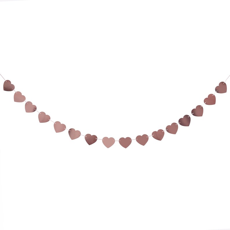 May include: A string of rose gold heart-shaped decorations hangs against a white background. The hearts are connected by a thin, white string, creating a festive garland. The hearts have a metallic sheen, reflecting light.