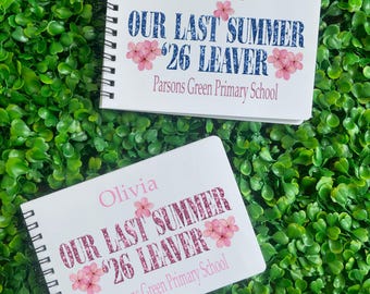 Op de afbeelding: Twee spiraalgebonden notitieboekjes met witte covers, met tekst en bloemaccenten. Het bovenste notitieboekje leest "Katie, OUR LAST SUMMER '26 LEAVER, Parsons Green Primary School." Het onderste notitieboekje leest "Olivia, OUR LAST SUMMER '26 LEAVER, Parsons Green Primary School."