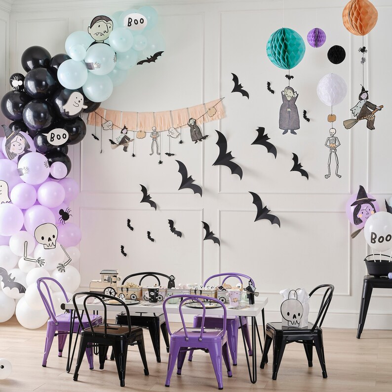 Peut inclure: Une sc&egrave;ne de f&ecirc;te d'Halloween avec des ballons noirs, violets et blancs, des chauves-souris en papier et des d&eacute;corations suspendues. Une table blanche est entour&eacute;e de chaises noires et violettes. Les d&eacute;corations incluent une banni&egrave;re avec des personnages d'Halloween.
