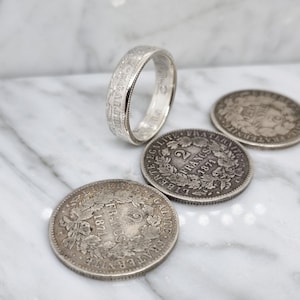 Könnte beinhalten: Ein silberner Ring, der aus einer 2-Franc-Münze aus dem Jahr 1871 gefertigt wurde. Der Ring wird mit drei weiteren 2-Franc-Münzen aus dem Jahr 1871 gezeigt.