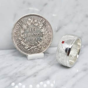 Peut inclure: Une bague en argent fabriquée à partir d'une pièce de 10 francs de 1866, avec une pierre précieuse rouge.