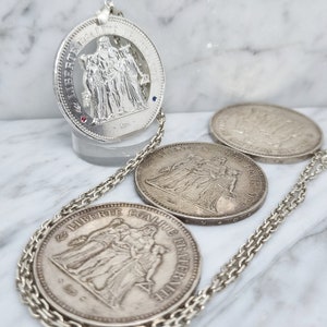 Peut inclure: Un collier en argent avec trois pièces de monnaie en argent représentant l'image de trois femmes. Les pièces sont gravées des mots "Liberté, Egalité, Fraternité".