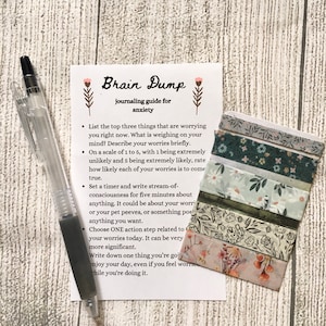 May include: A printable journaling guide for anxiety titled "Brain Dump". The guide includes prompts for identifying and processing worries, rating their likelihood, and taking action steps. The image also features decorative washi tape.