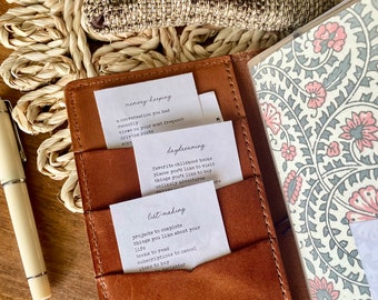 May include: A brown leather journal with three index cards inside. The index cards have handwritten text on them, including "memory-keeping", "daydreaming", and "list-making".