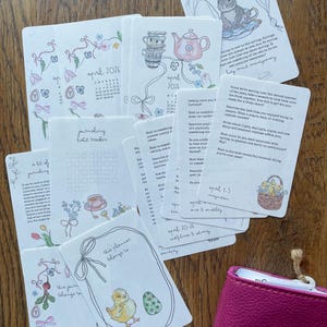 May include: A collection of illustrated planner cards and a pink planner. The cards feature floral and Easter-themed designs, including a bunny, chick, and teapot. Some cards have text like "April 2026" and "journaling habit tracker."