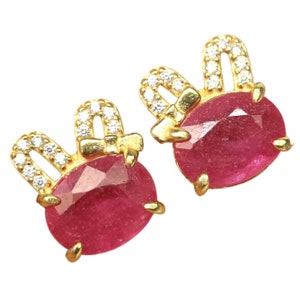 May include: A pair of gold earrings with a red gemstone and a white cubic zirconia bow design.