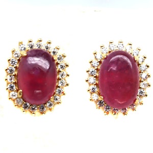 May include: A pair of gold earrings with a pink oval gemstone surrounded by a halo of smaller white gemstones.