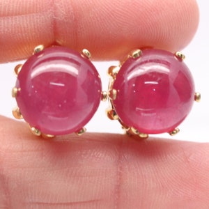 Op de afbeelding: Een paar gouden oorbellen met ovale roze robijnen.