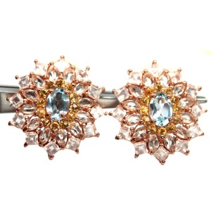 Op de afbeelding: Oorbellen van roségoud met een cluster van lichtroze, gele en blauwe edelstenen. De oorbellen hebben de vorm van een bloem.