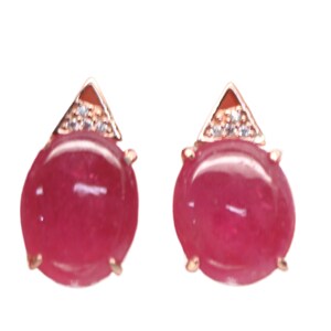 May include: A pair of ruby earrings with a triangular setting and small clear stones. The earrings are made of gold-toned metal.