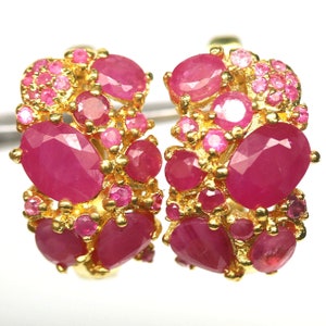 Op de afbeelding: Een paar gouden creolen met een cluster van roze robijn edelstenen. De oorbellen zijn gemaakt van 14 karaat goud en tonen een verscheidenheid aan robijn maten en vormen.