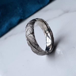 May include: A silver ring with a textured, hammered finish. The ring is made of metal and has a polished, shiny surface.
