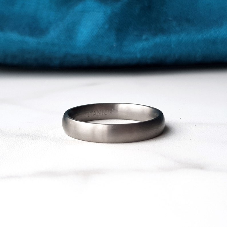 Op de afbeelding: Een geborstelde titanium trouwring met een eenvoudig, subtiel ontwerp. De ring is gegraveerd met het woord "TITANIUM".