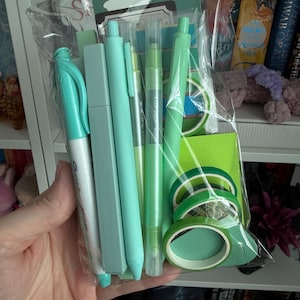 May include: A clear plastic bag containing a collection of mint green stationery items, including a Sharpie marker, a rectangular highlighter, two pens, and three rolls of washi tape. The packaging features a header card with the text BOOKS OF.