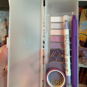 May include: A translucent plastic pencil case containing a set of stationery items including a purple pen, a dual-tip marker with Japanese text, a stack of gradient purple adhesive page markers, a roll of purple washi tape, and gold-toned metal clips.