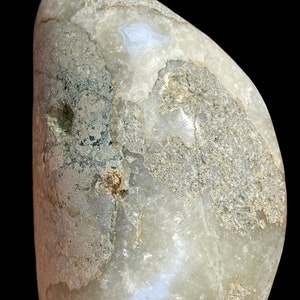 Puede incluir: Una piedra lisa de color gris claro, de forma ovalada, con un patr&oacute;n blanco y azul. La piedra tiene una superficie rugosa y texturizada con marcas verdes y marrones.