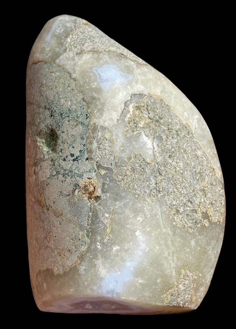 Puede incluir: Una piedra lisa de color gris claro, de forma ovalada, con un patr&oacute;n blanco y azul. La piedra tiene una superficie rugosa y texturizada con marcas verdes y marrones.