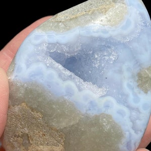 Puede incluir: Una geoda de &aacute;gata azul claro con una gran cavidad abierta. La geoda tiene un exterior rugoso y natural y un interior liso y pulido. La cavidad est&aacute; revestida de peque&ntilde;os cristales blancos.