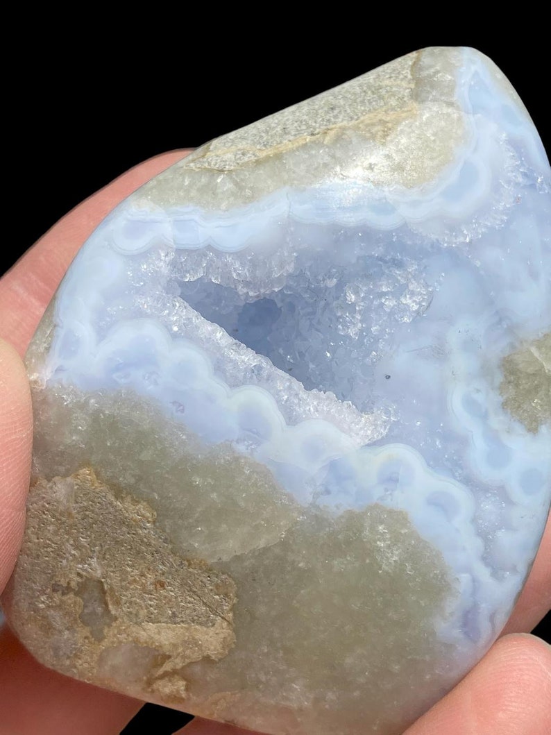 Puede incluir: Una geoda de &aacute;gata azul claro con una gran cavidad abierta. La geoda tiene un exterior rugoso y natural y un interior liso y pulido. La cavidad est&aacute; revestida de peque&ntilde;os cristales blancos.