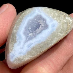 Puede incluir: Una geoda de &aacute;gata azul claro con un exterior blanco. La geoda est&aacute; cortada por la mitad, revelando el cristal en el interior.