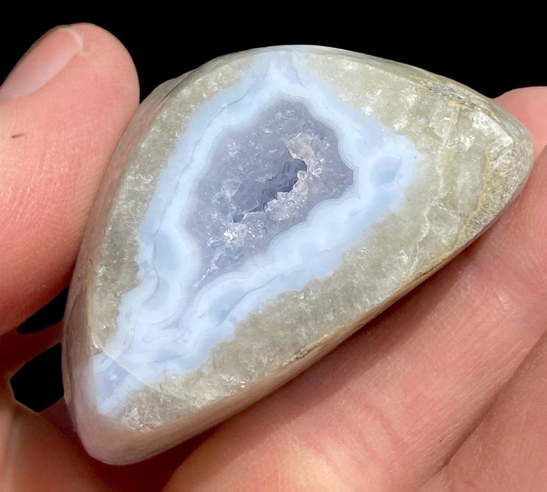 Puede incluir: Una geoda de &aacute;gata azul claro con un exterior blanco. La geoda est&aacute; cortada por la mitad, revelando el cristal en el interior.