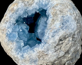May include: A geode with a rough, grey exterior encasing a cluster of light blue crystals. The crystals are visible in the centre, creating a striking contrast against the outer rock. The geode is a natural formation.