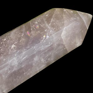 May include: A clear quartz crystal point with a faceted tip. The crystal has a pale, translucent appearance with subtle internal rainbows. The background is solid black, highlighting the crystal's form and clarity.