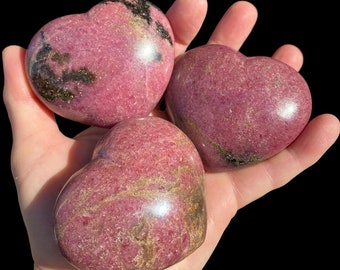 May include: Three pink and gold heart-shaped polished stones. The stones have a sparkly, glittery appearance.