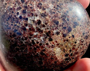 May include: A heart-shaped polished stone with a dark brown base and a speckled pattern of red and gold flecks.