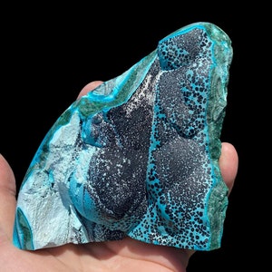May include: A large, irregularly shaped piece of blue and green chrysocolla with black inclusions. The stone has a smooth, polished surface and a variety of textures.
