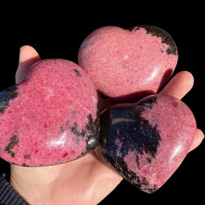 May include: Three pink and black heart-shaped polished stones. The stones have a marbled pattern of pink and black.