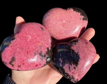 May include: Three pink and black heart-shaped polished stones. The stones have a marbled pattern of pink and black.
