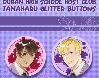 Może przedstawiać: Dwie okrągłe przypinki z ilustracjami postaci w stylu anime. Tekst głosi OURAN HIGH SCHOOL HOST CLUB TAMAHARU GLITTER BUTTONS. Jedna przypinka przedstawia postać z brązowymi włosami i czerwonymi różami, druga postać z blond włosami i fioletowymi różami, obie z brokatowym wykończeniem.