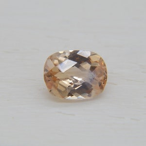 May include: A light peach-colored oval gemstone with a faceted cut.
