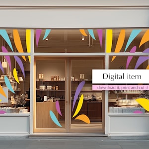 May include: Exterior shot of a storefront with a white facade and large glass windows. The windows are decorated with colorful abstract shapes in yellow, orange, purple, and teal. Text on the window reads "Digital item" and "download it, print and cut ;)".