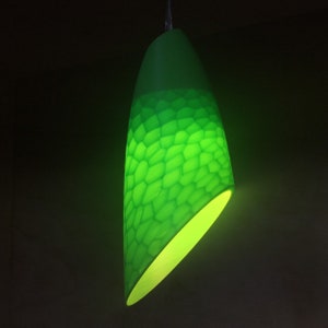 Puede incluir: Una lámpara colgante verde con un patrón de panal. La luz está encendida e ilumina la habitación con un brillo cálido.