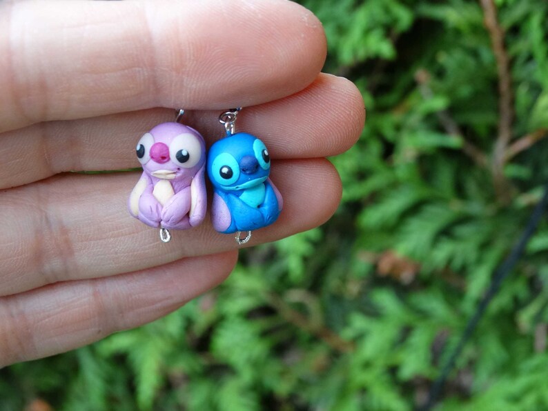 May include: A pair of handmade polymer clay earrings featuring Stitch and Angel from the Disney movie Lilo & Stitch. The earrings are blue and purple and have silver hooks.