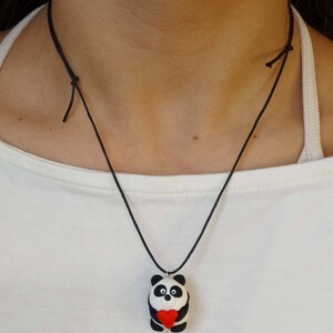K&ouml;nnte beinhalten: Eine schwarze Schnurkette mit einem wei&szlig;en und schwarzen Pandabanh&auml;nger, der ein rotes Herz h&auml;lt. Der Pandabanh&auml;nger ist aus Polymer Clay.