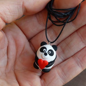 K&ouml;nnte beinhalten: Eine schwarze Schnurkette mit einem Panda-Anh&auml;nger, der ein rotes Herz h&auml;lt. Der Panda ist aus wei&szlig;em und schwarzem Fimo gefertigt.