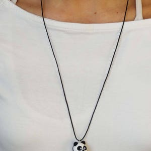 K&ouml;nnte beinhalten: Eine schwarze Schnurkette mit einem wei&szlig;en und schwarzen Pandab&auml;ren-Anh&auml;nger, der ein rotes Herz h&auml;lt.