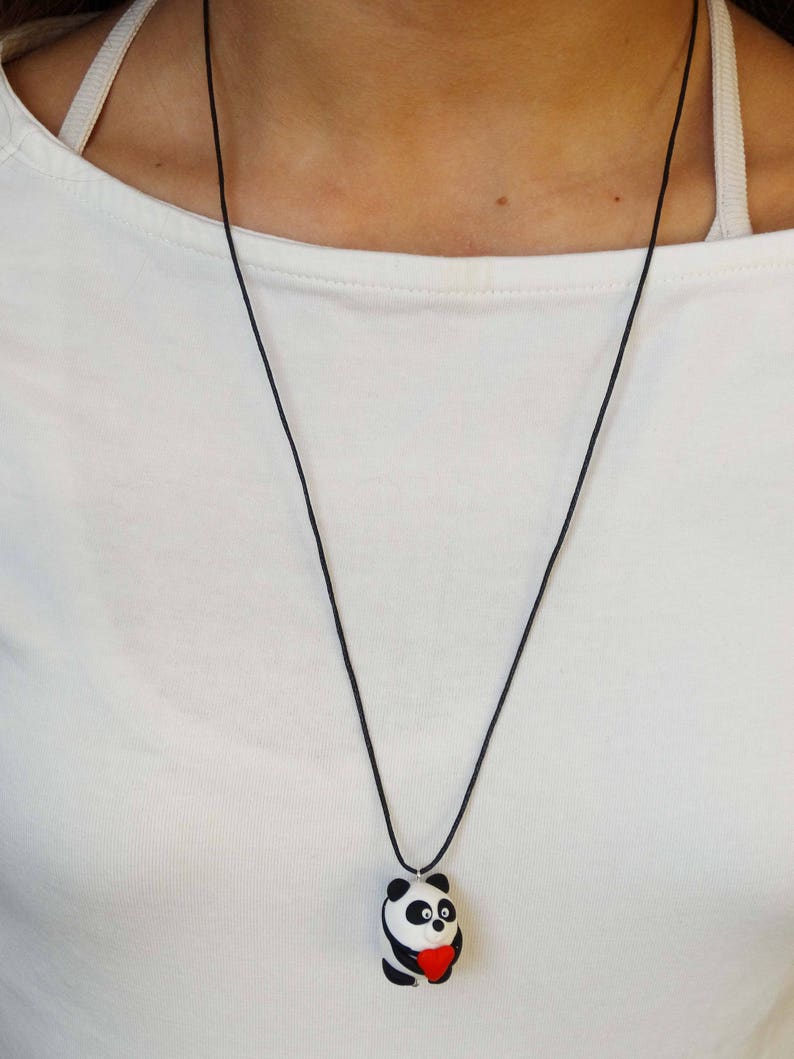 K&ouml;nnte beinhalten: Eine schwarze Schnurkette mit einem wei&szlig;en und schwarzen Pandab&auml;ren-Anh&auml;nger, der ein rotes Herz h&auml;lt.