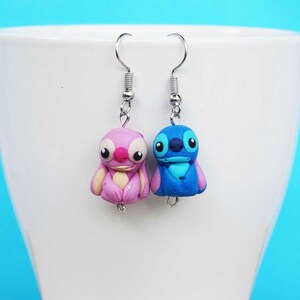 May include: A pair of dangle earrings featuring Stitch and Angel from the Disney movie Lilo & Stitch. The earrings are made of polymer clay and have silver hooks.