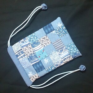 May include: A blue drawstring bag made of patchwork fabric with a variety of blue and white patterns. The bag has a simple design and is perfect for carrying small items.