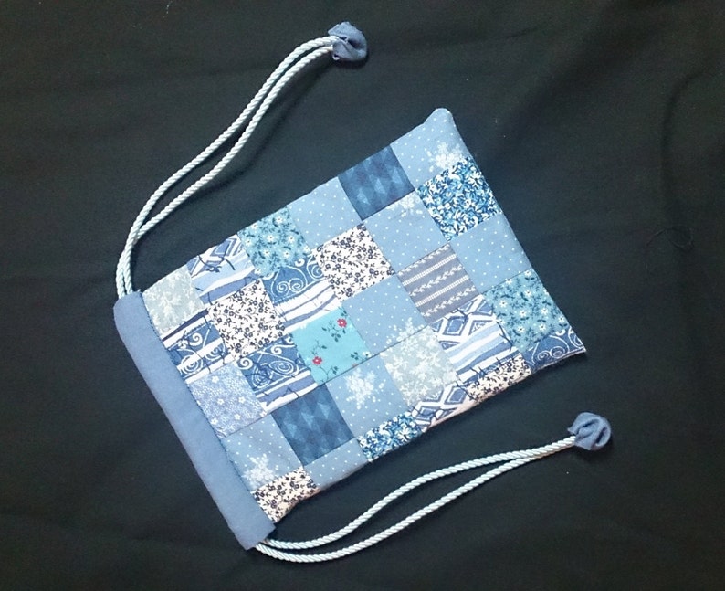 May include: A blue drawstring bag made of patchwork fabric with a variety of blue and white patterns. The bag has a simple design and is perfect for carrying small items.